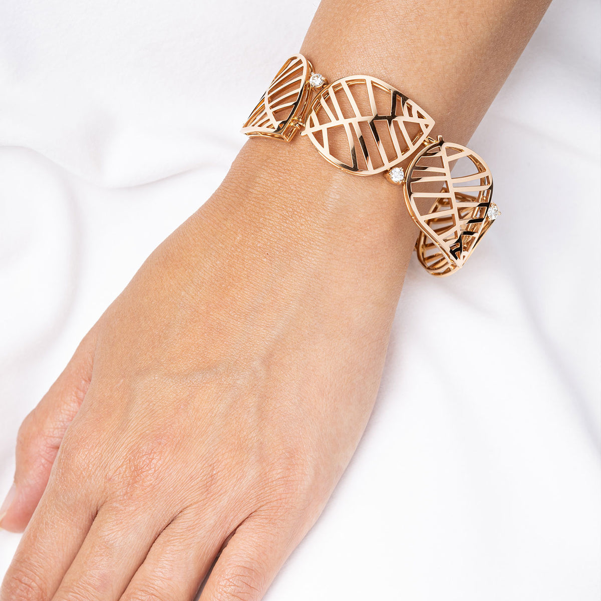 Woman wearing an 18k rose gold bracelet with openwork leaf design and pave diamonds, De Parme Design