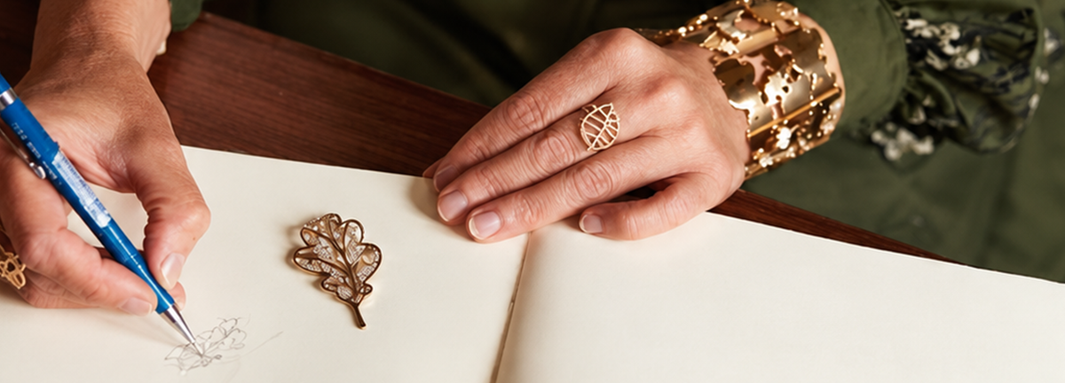 Princess Margarita sketching an oak leaf in her notebook, next to a gold oak leaf brooch and her Oak collection ring and cuff